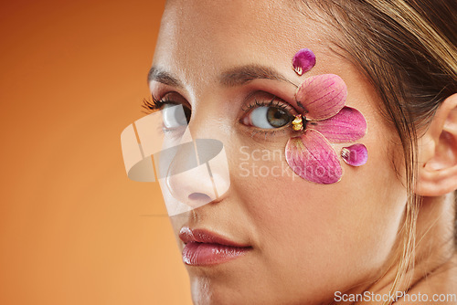 Image of Model, flower and eye for makeup at studio for art, portrait and natural beauty. Woman, flowers and eyes with floral organic cosmetics on skin with glow, shine and healthy face with orange background