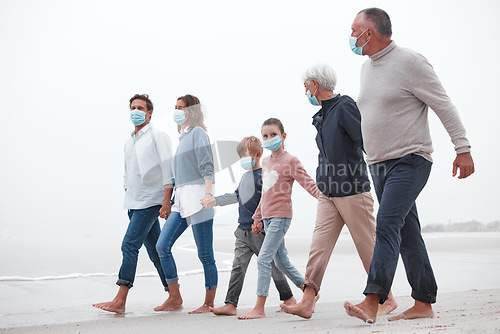 Image of Covid, mask and big family walking together on a beach with mother, father and children outdoor. Parents, kids and grandparents walking on sand at the ocean water waves holding hands with love