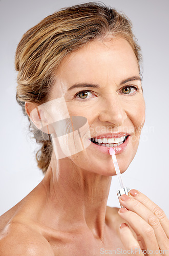 Image of Cosmetics, lip gloss and senior woman for wellness, natural beauty and healthy with grey studio background. Portrait, makeup and elderly female with smile, confident and happy with hydrate product.