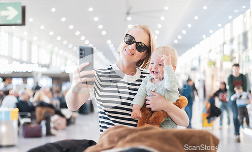 Image of Mother taking selfie with mobile phone, while traveling with child, holding his infant baby boy at airport, waiting to board a plane. Travel with kids concept.