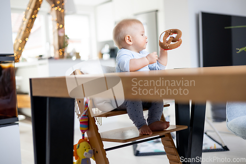 Image of Happy infant sitting at dining table and playing with his toy in traditional scandinavian designer wooden high chair in modern bright atic home. Cute baby playing with toys