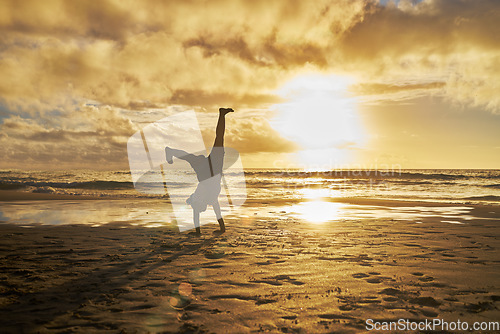 Image of Sunset, silhouette and child doing cartwheel at the beach having fun, playing and enjoy nature. Freedom, inspiration for youth and kid doing handstand by ocean on summer vacation, holiday and weekend