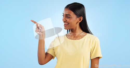 Image of Woman, pointing and deal with marketing, information and direction for announcement in studio. Blue background, person and promotion with smile and sale with offer and show hand sign of student