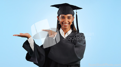 Image of Graduation, portrait and happy woman point, palm gesture and advertising learning, university info or college study. Studio mockup space, student commercial ads or school graduate on blue background