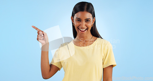 Image of Woman, pointing and portrait with marketing, advertising and direction for announcement in studio. Blue background, person and promotion with smile and sale with offer and show hand sign of student