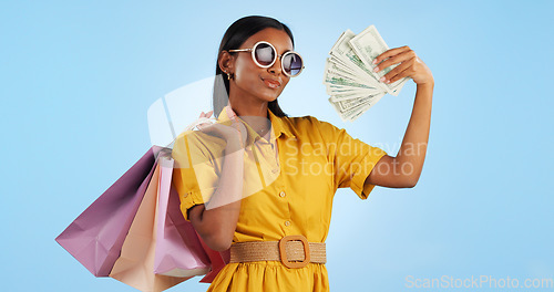 Image of Woman, shopping bag and money fan, wealth and commerce with customer in sunglasses on blue background. Cash, financial freedom and retail, fashion and product choice, rich and shop discount in studio