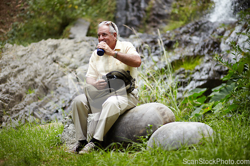 Image of Senior, man and drinking water in forest for break, sightseeing or vacation with waterfall and scenery. Elderly person in woods or nature to rest on holiday, adventure or experience with backpack