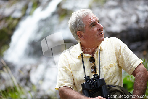 Image of Senior, man and binocular in forest with looking, sightseeing or vacation with waterfall and scenery. Elderly, man and person in woods or nature for holiday, adventure or experience for leisure