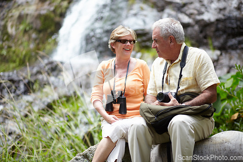 Image of Senior, man and woman with binocular for travel, sightseeing or holiday with happiness on rocks. Elderly, couple and face with smile for waterfall, vacation and adventure on retirement or tourism