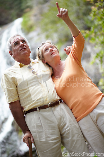 Image of Senior, man and woman with pointing in forest for travel, sightseeing or holiday with waterfall. Elderly, couple or face and showing view for vacation and adventure on retirement or tourism in nature