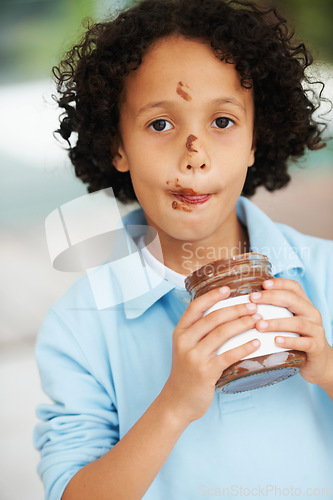 Image of Cute, portrait and child with chocolate spread at a home with delicious, sweet snack or treat. Smile, happy and face of young boy kid from Mexico eating nutella jar licking lips at modern house.