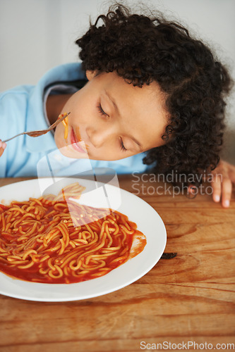 Image of Hungry, food and child eating spaghetti by the wooden kitchen counter for lunch at home. Pasta, tomato and boy kid enjoying a meal for dinner or supper for nutrition at a table in a modern house.