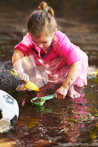 Image of Girl, child and play with toys in mud for freedom, activity and muddy fun in sunshine weather or outdoor. Kid, female and river of person with peace for playing, enjoyment and relax in dirt water