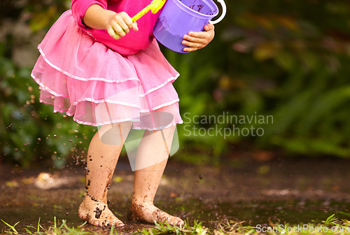 Image of Legs, girl and kid with toy bucket in muddy puddle for play, explore and child development in garden or backyard. Person, feet or toys in mud water for activity, playing and freedom outdoor in nature