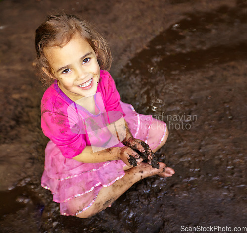 Image of Girl, child and portrait with happiness in mud for freedom, playing and muddy fun in sunshine weather or outdoor. Kid, female and face of person with smile for activity, enjoyment and relax in dirt