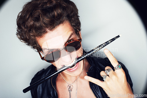 Image of Rock man, horns and studio portrait with drumstick, sunglasses or biting in spotlight by white background. Punk musician, drummer or artist with emoji, icon and hand sign for performance at concert