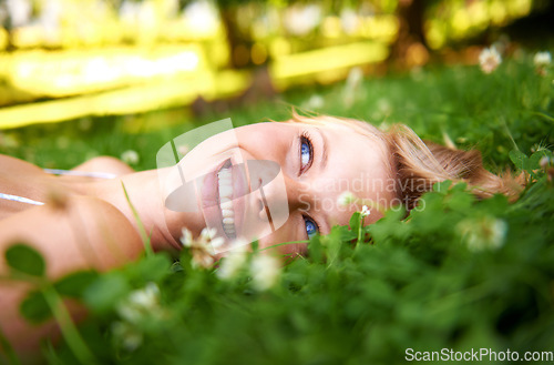 Image of Spring, happy and calm with woman on grass in nature for relax, smile and peace. Park, flowers and field with face of female person lying in countryside meadow for summer, vacation and wellness