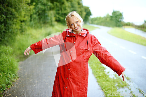 Image of Woman, smile and raincoat in rain with arms, wet and cold from weather, winter and nature. Happy female person, fashion and red jacket in storm, rainfall and protection from water, face and outdoors