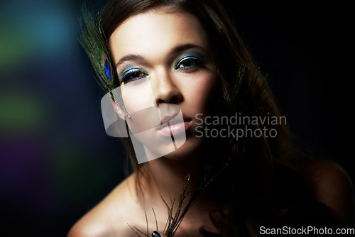 Image of Portrait, makeup and peacock feather with a woman in studio on dark background for natural skincare or wellness. Face, skin or beauty and a confident young model looking creative with cosmetics