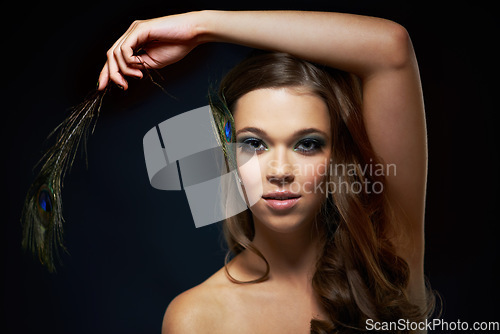 Image of Portrait, skincare and peacock feather with a woman in studio on dark background for natural skin or wellness. Face, beauty or makeup and arm of a young model looking creative with artistic cosmetics