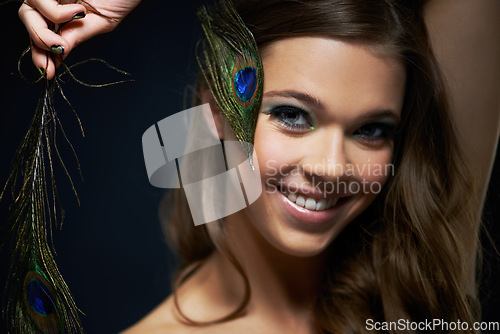 Image of Portrait, beauty and peacock feather with a woman in studio on dark background for natural skincare or wellness. Face, skin or makeup and a happy young model looking creative with artistic cosmetics