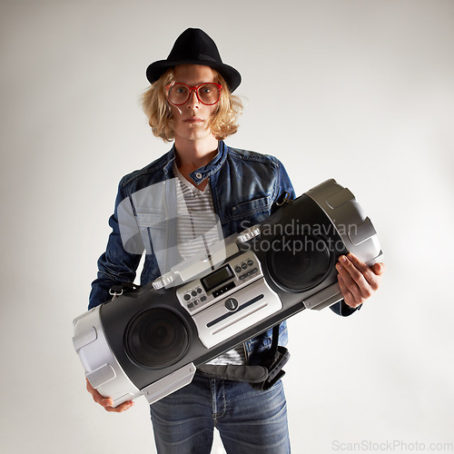 Image of Boombox, fashion and portrait of a man in studio with music, radio or audio sound. Serious model person on grey background with denim outfit, glasses and hipster hat or retro style to listen to song