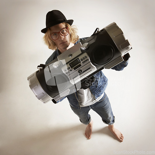 Image of Boombox, portrait and fashion of a man in studio with music, radio or audio sound and above. Serious model person on a grey background with denim outfit, glasses and hipster hat to listen to song