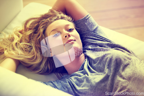 Image of Portrait, relax and a woman on a sofa in the living room of her home on the weekend with a lighting filter. Peace, wellness and a happy young teen girl lying alone in her apartment for morning rest