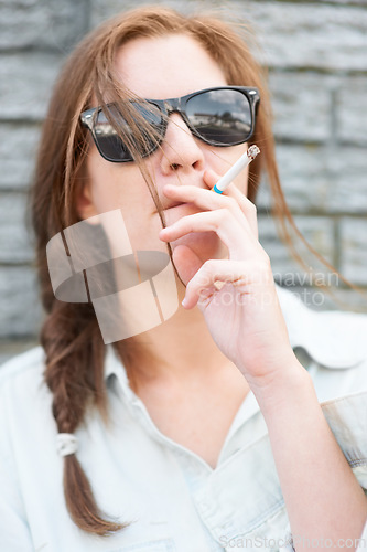 Image of Cool, city and a woman with sunglasses smoking with streetwear, stylish and urban culture. Fashion, young and a girl with a smoke, cigarette or enjoying a smoker habit to relax on the weekend