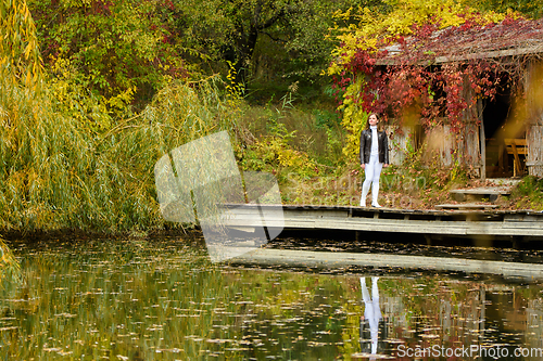 Image of A young beautiful girl walks by the lake in an autumn park