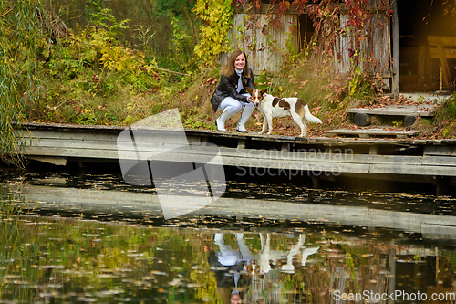 Image of A young beautiful girl walks with a dog near a lake in an autumn park