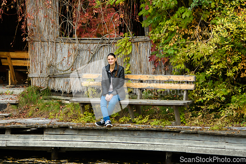 Image of A young beautiful girl in casual clothes sits on a bench in an autumn park