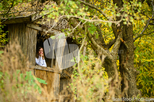 Image of A young beautiful girl looks out of the window of an old abandoned house in the forest