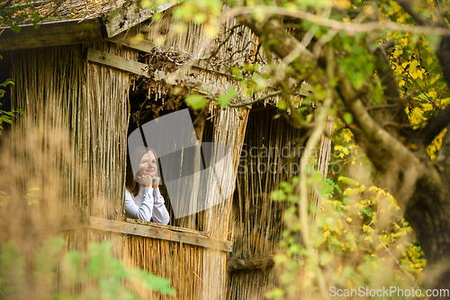 Image of A young beautiful girl looks out of the window of an old house in the forest