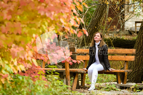 Image of A young beautiful girl sits on a bench and enjoys the autumn landscape