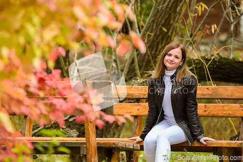 Image of A young beautiful girl sits on a bench in an autumn park