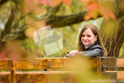 Image of A young beautiful girl sits on a bench in an autumn park and turns around and looks into the frame.
