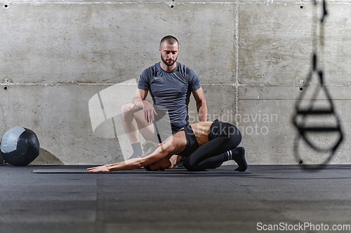 Image of A muscular man assisting a fit woman in a modern gym as they engage in various body exercises and muscle stretches, showcasing their dedication to fitness and benefiting from teamwork and support