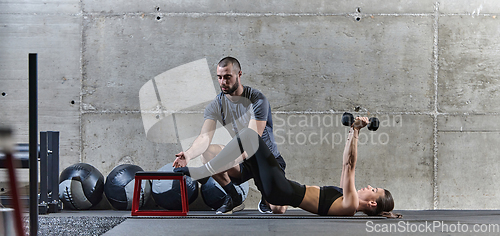 Image of A muscular man assisting a fit woman in a modern gym as they engage in various body exercises and muscle stretches, showcasing their dedication to fitness and benefiting from teamwork and support