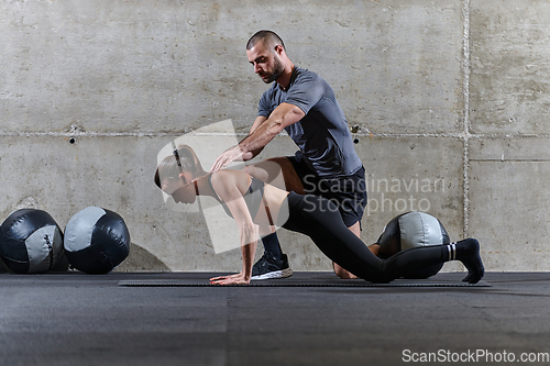 Image of A muscular man assisting a fit woman in a modern gym as they engage in various body exercises and muscle stretches, showcasing their dedication to fitness and benefiting from teamwork and support