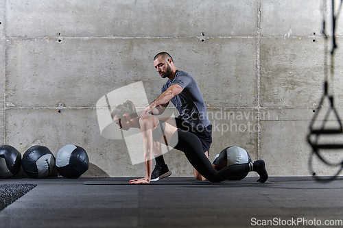 Image of A muscular man assisting a fit woman in a modern gym as they engage in various body exercises and muscle stretches, showcasing their dedication to fitness and benefiting from teamwork and support