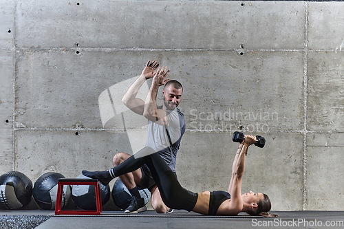 Image of A muscular man assisting a fit woman in a modern gym as they engage in various body exercises and muscle stretches, showcasing their dedication to fitness and benefiting from teamwork and support