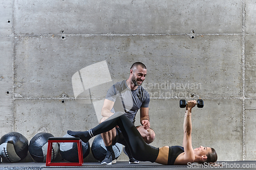 Image of A muscular man assisting a fit woman in a modern gym as they engage in various body exercises and muscle stretches, showcasing their dedication to fitness and benefiting from teamwork and support