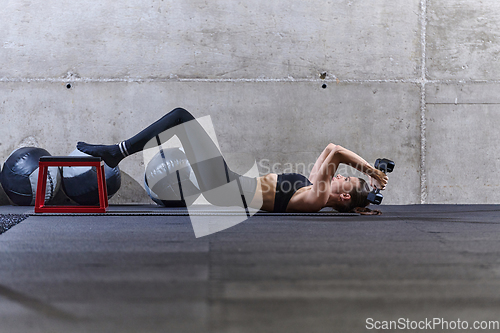 Image of A fit woman is lying on the gym floor, performing arm exercises with dumbbells and showcasing her dedication and strength.