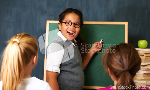 Image of Excited, board and portrait of child student in a classroom teaching a lesson to friends. Happy, smile and girl kid writing with chalk for education studying, learn or knowledge at school or academy.