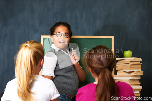 Image of Teaching, smile and portrait of kid student by board for lesson, knowledge or education with friends. Happy, glasses and girl child talking and writing with chalk for classmates in school or academy.