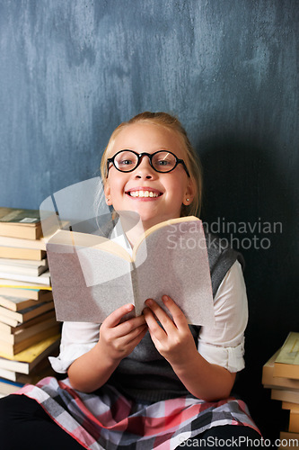 Image of Girl reading book, student and chalkboard for education, language learning and knowledge in classroom. Smart kid or child with glasses and happy for school library, fiction and literature in portrait