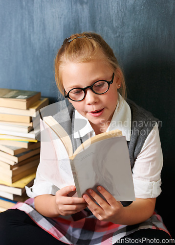 Image of Child, student reading book and chalkboard for education, language learning and knowledge in classroom. Smart girl or storytelling in glasses and school library, creative development and literature
