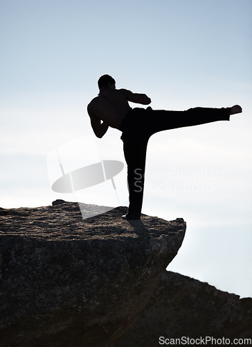 Image of Karate, kick and fitness man on mountain top for body, power or defense training on blue sky background. Martial arts, MMA and male taekwondo master in nature for exercise, sports or morning cardio