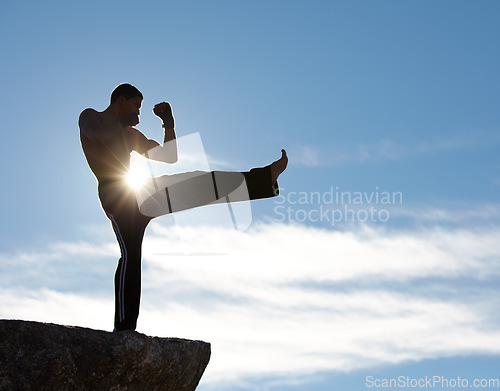 Image of Karate, fitness man kick on mountain top for body, power or defense training on blue sky background. Martial arts, MMA and male taekwondo master in nature for exercise, sports or morning cardio